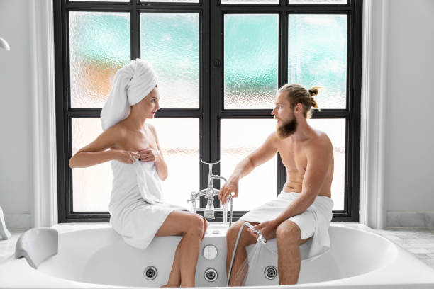 coppia maschile e femminile indossare asciugamani sta mostrando amore l'uno per l'altro. alla vasca da bagno nel bagno con una grande finestra. - bathroom bathtub heterosexual couple male beauty foto e immagini stock