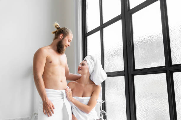 coppia maschile e femminile indossare asciugamani sta mostrando amore l'uno per l'altro. alla vasca da bagno nel bagno con una grande finestra. - bathroom bathtub heterosexual couple male beauty foto e immagini stock