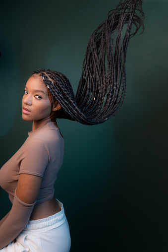 Beautiful young woman, sitting sideways, with braids of her hair flying. Isolated on dark cyan background.