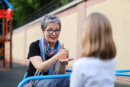 Mature woman speaks sign language with a small child girl on the playground.