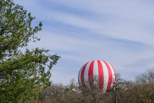 red and white hot air balloon flying in the sky around trees in the park