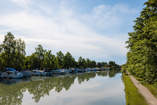 Wide shot of a canal in Toulouse in the South of France. There are moored riverboats next to the trees.