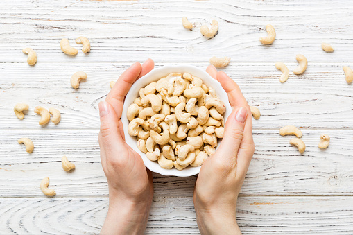 Woman hands holding a wooden bowl with cashew nuts. Healthy food and snack. Vegetarian snacks of different nuts.