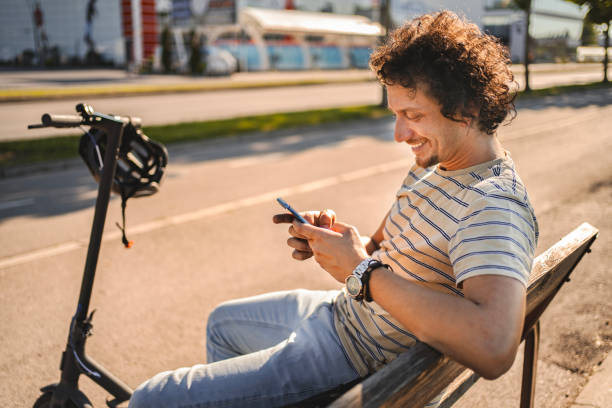 istock Man sitting on the bench looking at his phone while taking a break from riding his electric scooter 1511458531
