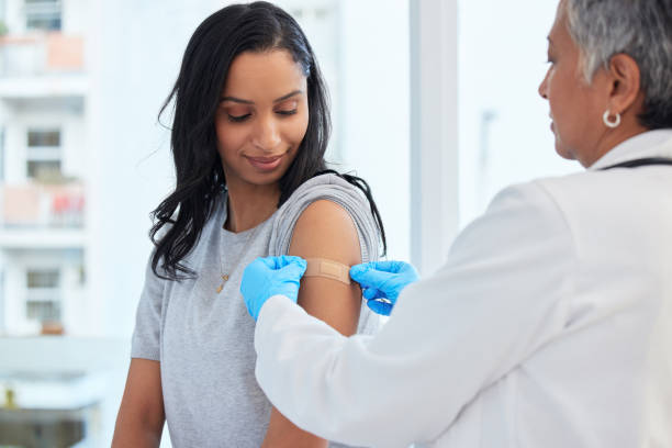 Healthcare, woman and doctor with plaster, vaccination and consultation in a hospital, cure and disease. Female patient, client and medical professional with care, vaccine and injection for safety stock photo