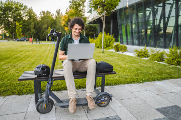 istock Men working on his laptop while sitting on a bench beside his electric scooter 1511470964