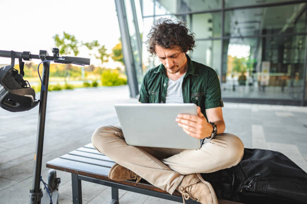 istock Men working on his laptop while sitting on a bench beside his electric scooter 1511473093