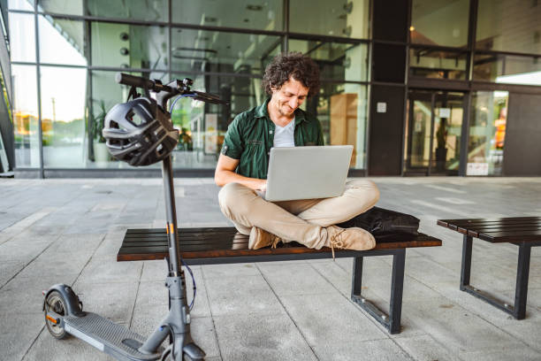 istock Men working on his laptop while sitting on a bench beside his electric scooter 1511473627