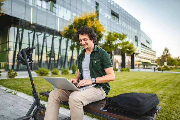 istock Men working on his laptop while sitting on a bench beside his electric scooter 1511475193