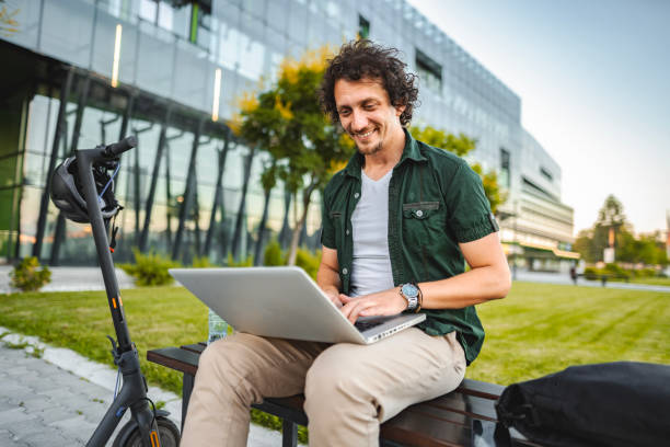 istock Men working on his laptop while sitting on a bench beside his electric scooter 1511475195
