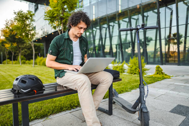 istock Men working on his laptop while sitting on a bench beside his electric scooter 1511478365