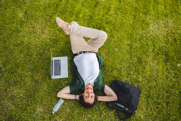 istock Men lying on the grass in public park while taking a break from working on his laptop 1511480523