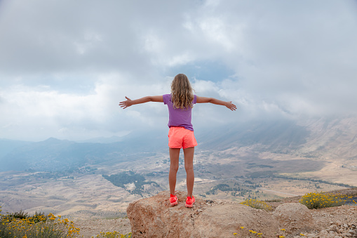 Joyful teen girl with raised up hands. Enjoying gorgeous view on high mountains. Happy summer vacation.