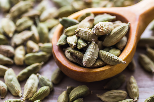 Green cardamom in a wooden scoop, an aromatic spice used in the kitchen, providing many health benefits.
