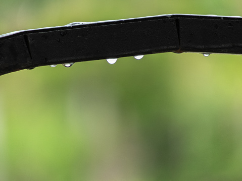 single water drop, teetering on the edge of an iron surface, defies gravity before succumbing to its weight and gracefully plummeting, leaving behind fleeting trace of moisture as it meets the ground.