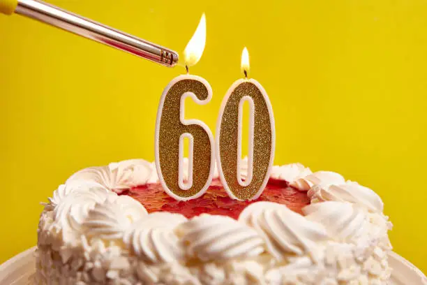 A candle in the form of the number 60, stuck in a festive cake, is lit. Celebrating a birthday or a landmark event. The climax of the celebration.