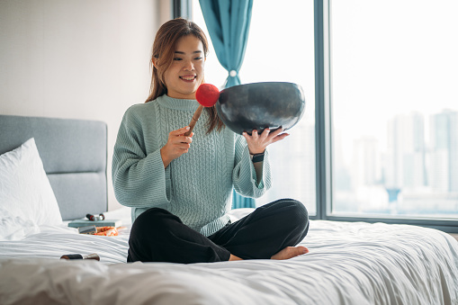 Beautiful young Asian woman meditating with a singing bowl at bedroom.