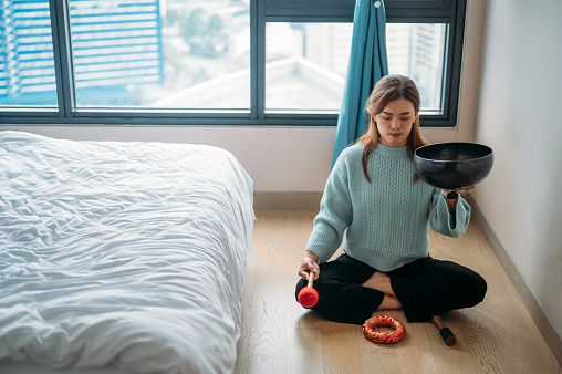 Beautiful young Asian woman meditating with a singing bowl at bedroom.