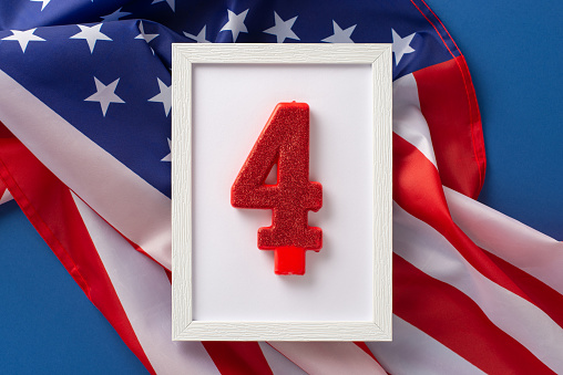The fourth of july celebration concept. Above view photo wooden frame with the glitter number 4 surrounded by an american flag on blue isolated background