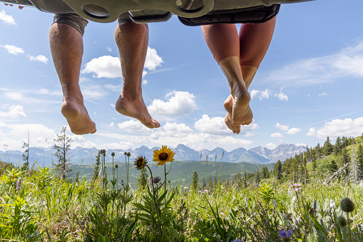 They are sitting on the back of their vehicle and dangling legs off the edge and above a mountain meadow, Crowsnest Pass, Alberta