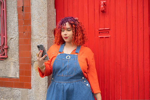 Young adult with colour hair holding smartphone against red door