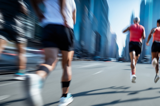 The blurred motion of a group of marathon runners as they run on an urban street. Everyone is unrecognizable by the blur of the motion.