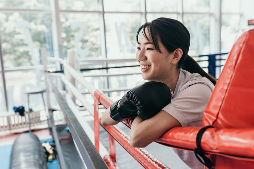 Young Asian woman boxer standing in one corner of a ring. have a rest after hard training at a sports gym