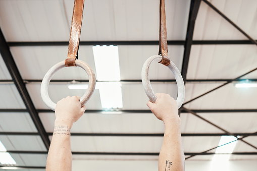 Hands, rings and gymnastics in fitness for workout, strength training or practice at gym. Hand of athlete, gymnast or acrobat holding or hanging on ring circles for strong intense pull up exercise