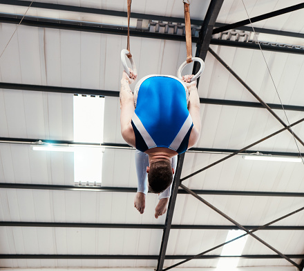 Man, acrobat and gymnast turning on rings in fitness for practice, training or workout at gym. Professional male gymnastics hanging on ring circles for athletics, balance or strength exercise indoors