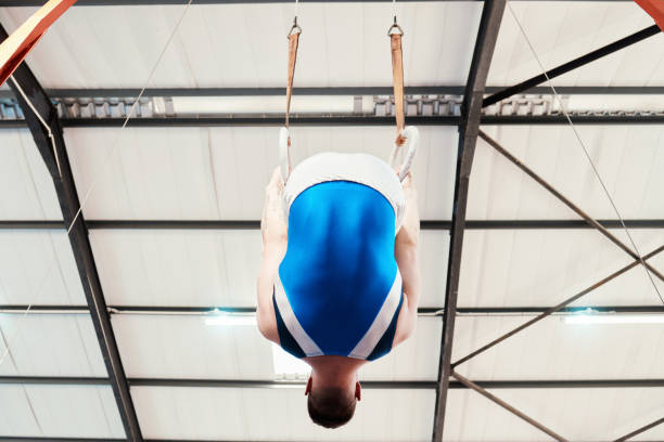 Man, acrobat and gymnastics on rings in fitness for practice, training or workout performance at gym. Professional male gymnast hanging on ring circles for athletics, acrobatics or strength exercise hombre, acróbata y gimnasia en anillos en fitness para la práctica, entrenamiento o entrenamiento de rendimiento en el gimnasio. gimnasta profesional masculino colgado en círculos de ring para atletismo, acrobacias o ejercicios de fuerza