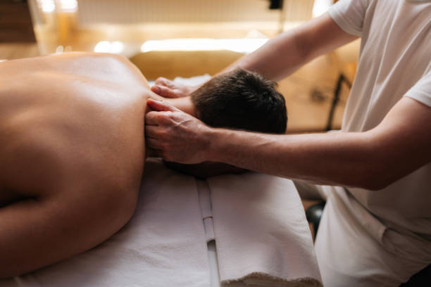 vista lateral de primer plano de la cabeza de un joven relajado irreconocible acostado en una mesa de masaje durante el masaje de hombros y cuello en el salón de spa. - massage therapist massaging sport spa treatment fotografías e imágenes de stock