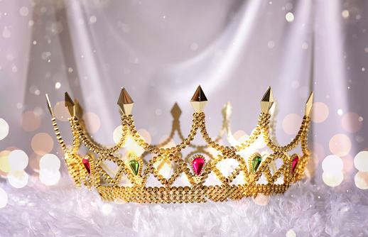 Beautiful golden crown with gems on white fluffy cloth, bokeh effect