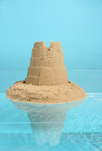 Pile of sand with tower on rippled water against light blue background. Beautiful castle