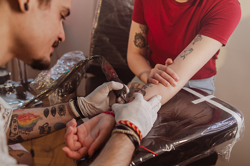 Portrait of a concentrated male tattoo artist tattooing on his client's arm