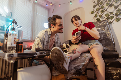 Portrait of a handsome tattoo artist and his female client getting tattoo ideas on the internet