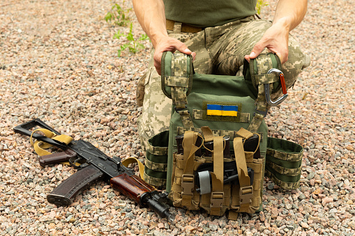 A soldier in a camouflage tactical uniform and a military body armor on a brown background. Bulletproof vest with combat stocks. Ukrainian army. Military concept. No war.