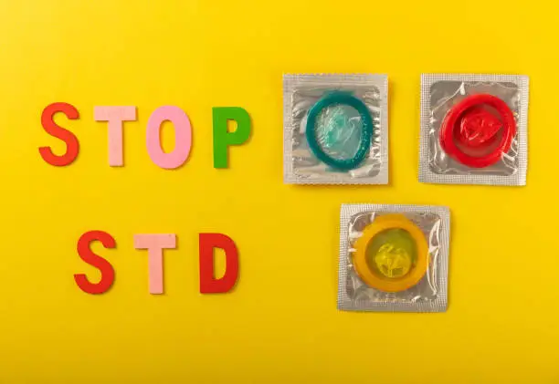 Colorful blocks with "STOP STD" phrase background, flat lay. Super safe strawberry condoms with a pleasant smell on a yellow background. Contraceptives are made from natural rubber latex