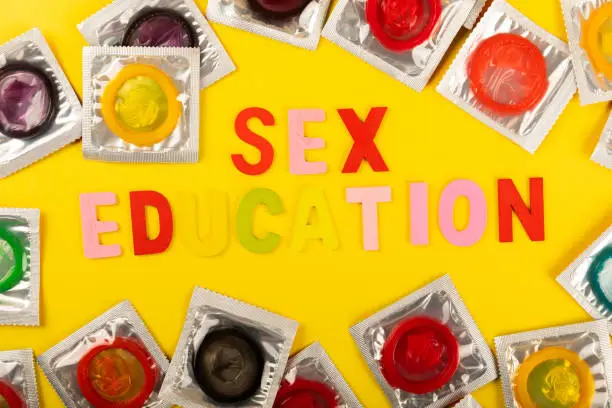 Colorful blocks with the phrase "SEX EDUCATION" background, flat lay. Super safe strawberry condoms with a pleasant smell on a yellow background. Contraceptives are made of natural rubber latex, high