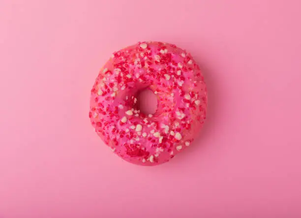 Donut on a pink background.Strawberry donut with pink icing and sprinkles on a paper background.Colorful minimalism concept.Junk food.Sweets.Copy space.Flat lay.Place for text.