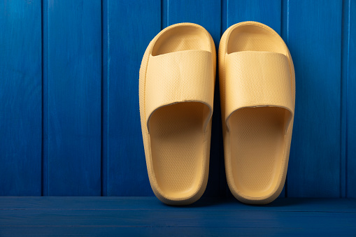 Yellow rubber summer slippers. Replacement shoes for home or office. Yellow slippers on a background of blue space. Relax concepts. Space for text.Space for copy.