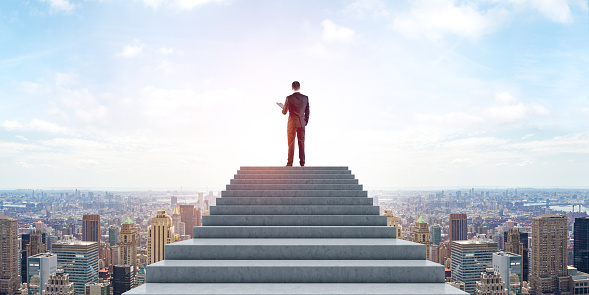 Businessman climbed the stairs with clipboard in hand, panoramic New York cityscape under blue sky. Concept of business goal, achievement, career development and success