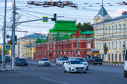 Russia, Tula - July 24, 2022: Cars drives on Sovetskaya street in a sunny summer day. Red building with green roof of Tula Military Prosecutor's Office in the background. City life theme.