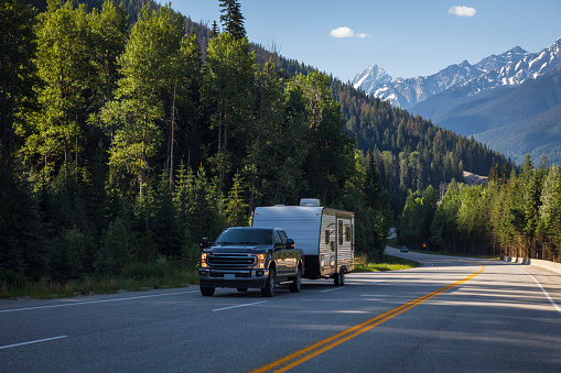 Pickup truck and camping trailer on the Trans-Canada Highway in the beautiful wilderness landscape of the Canadian Rockies of Banff National Park in Alberta, Canada.