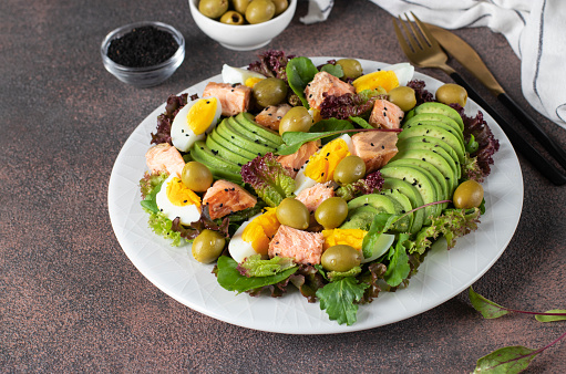Salad with baked salmon, avocado, eggs and olives, sprinkled with sesame seeds on a white plate