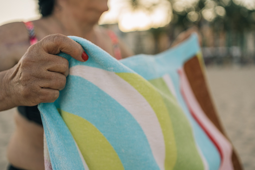 Hands of retired senior woman stretching and shaking her beach towel. Close-up image of an unrecognizable senior lady on vacation picking up the towel after having removed the sand by waving it.