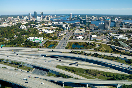Aerial view of Jacksonville city with high office buildings and american freeway intersection with fast driving cars and trucks. View from above of USA transportation infrastructure.