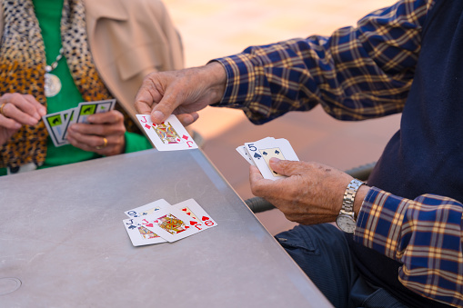 Hands of two elderly people in the garden of a nursing home or retirement home playing cards on a summer morning
