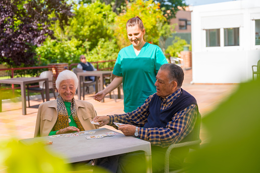 Dos personas mayores con la enfermera en el jardín de una residencia de ancianos o de retiro jugando a las cartas en una mañana de verano photo