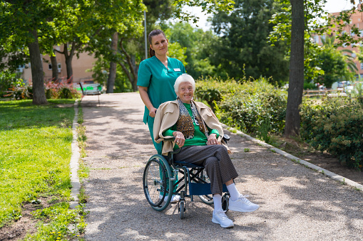 Portrait of an elderly woman with the nurse on a walk in the garden of a nursing home in a wheelchair