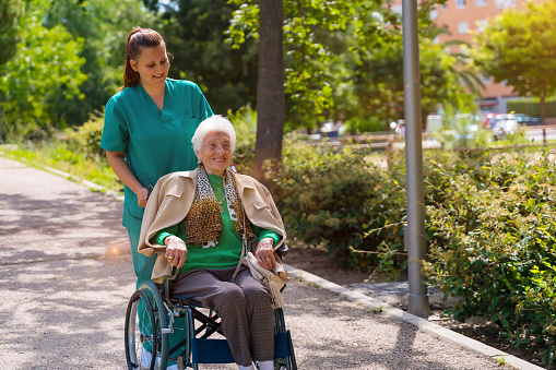 An elderly woman with the nurse on a walk in the garden of a nursing home in a wheelchair next to nature